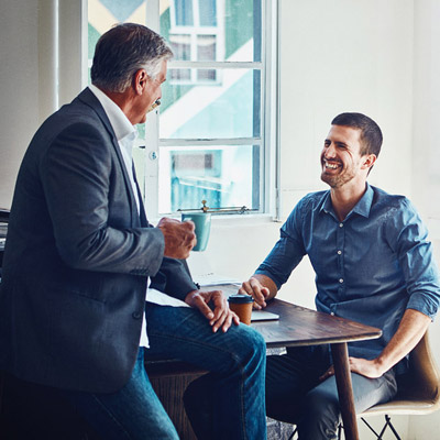 Two colleagues seated at a small table in a bright office, talking.