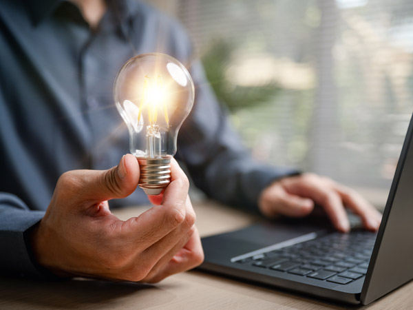 Oakford Group research-led approach to innovation, holding a lit bulb beside a laptop, in residential property operations across Southern England